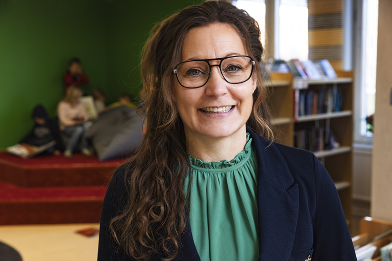 Rektor Kristin Nilsson står i ett bibliotek i sin arbetsmiljö