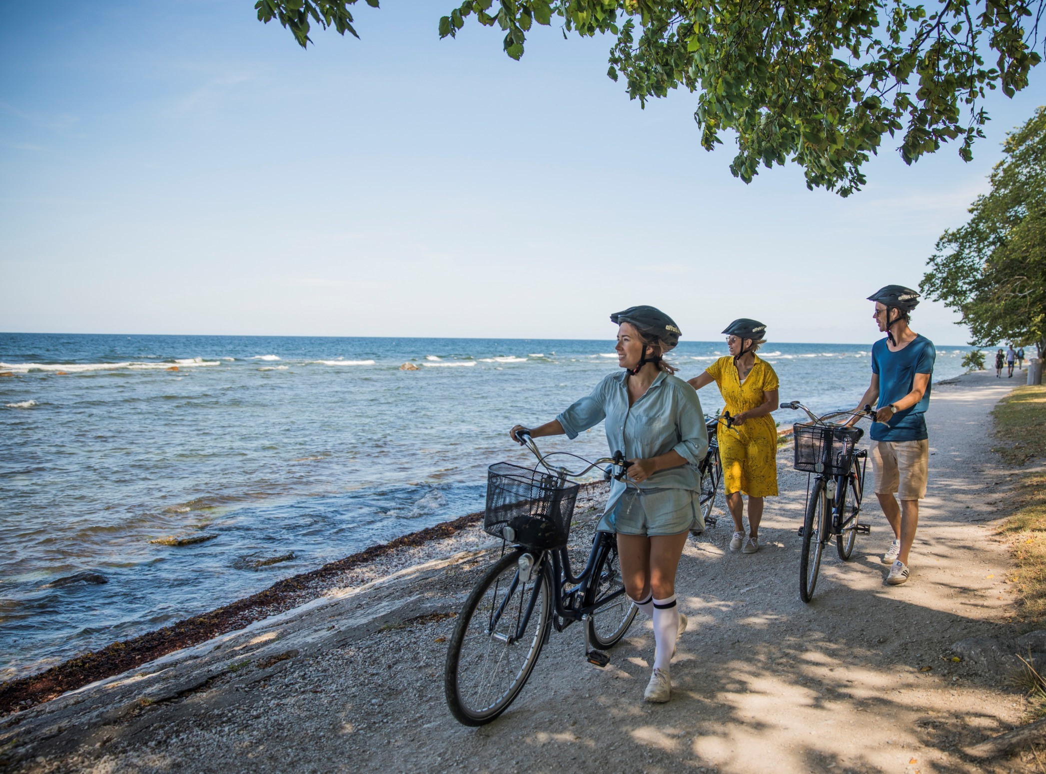 Tre personer leder sina cyklar längs strandpromenaden i Visby