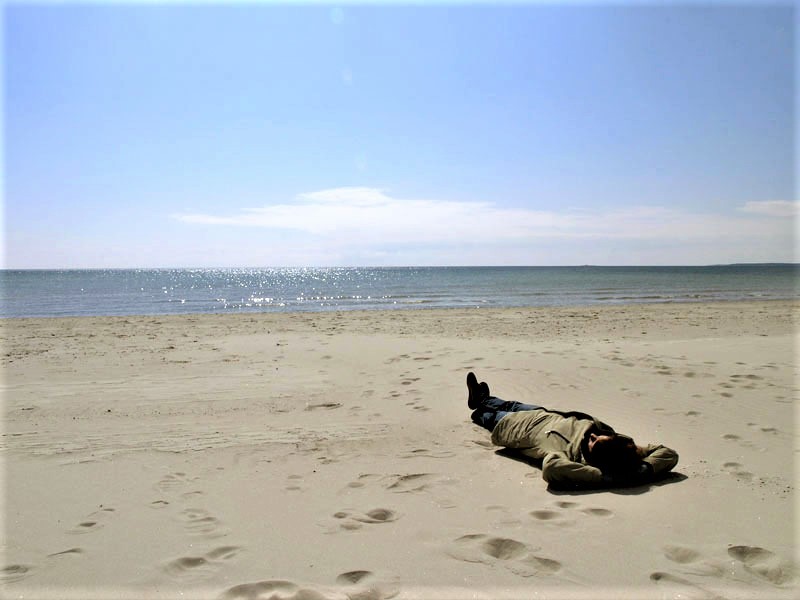 Kvinna i vinterkläder ligger på sanden på en strand en solig vårvinterdag
