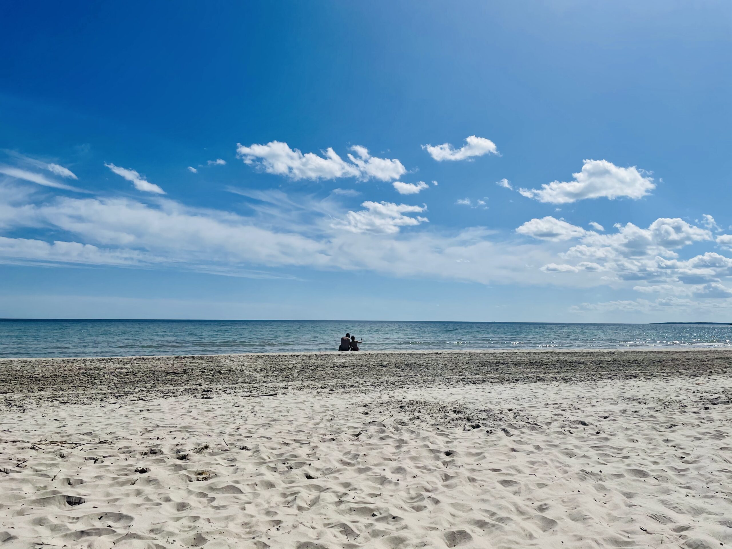 Pappa och son sitter vid strandkanten på Sudersand