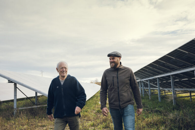 Två män vandrar mot kameran och i bakgrunden syns en solcellspark